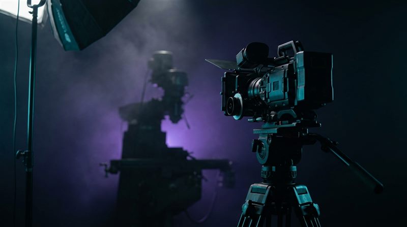 Cinema camera on a tripod and the silhouette of a machine on a dark set